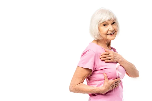Старша жінка дивиться на камеру, торкаючись грудей ізольовано на білому, концепція раку молочної залози — стокове фото