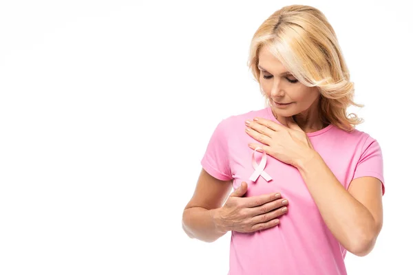 Mulher loira tocando no peito e olhando para fita rosa de consciência do câncer isolado no branco — Fotografia de Stock