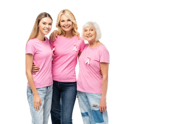 Mujeres en camisetas de color rosa con cintas de sensibilización sobre el cáncer de mama abrazando y mirando a la cámara aislada en blanco - foto de stock