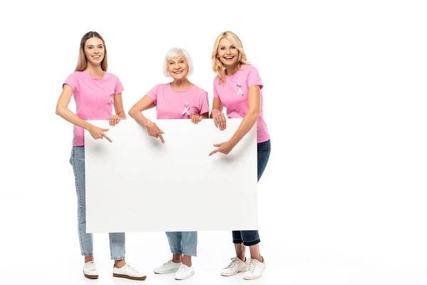 Mujeres con cintas rosas de conciencia sobre el cáncer de mama en camisetas apuntando a tablero vacío sobre fondo blanco - foto de stock