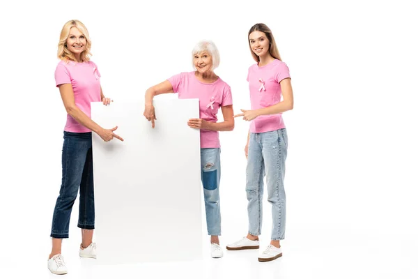 Mujeres en camisetas rosas apuntando a tablero vacío sobre fondo blanco, concepto de cáncer de mama - foto de stock