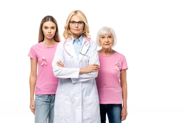 Médico com braços cruzados de pé perto de mulheres com fitas rosa em camisetas isoladas em branco — Fotografia de Stock