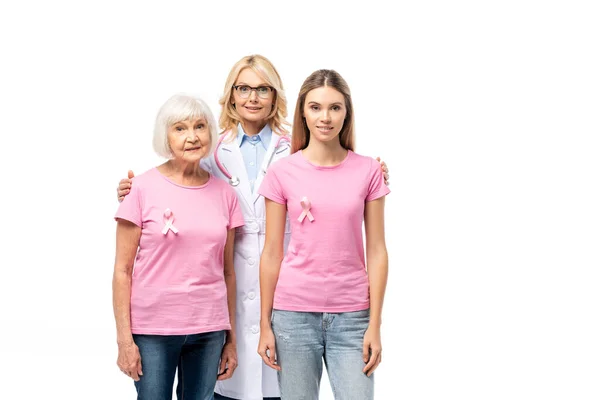 Médico abrazando a las mujeres con cintas rosas en camisetas aisladas en blanco - foto de stock