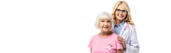 Foto panorámica de médico abrazando a mujer mayor con cinta rosa aislada en blanco - foto de stock