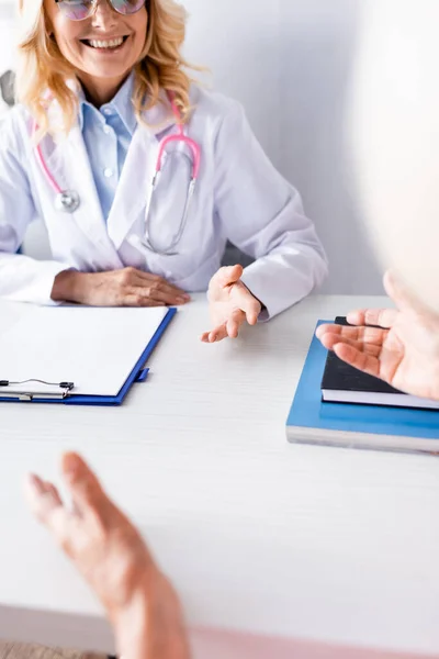 Selective focus of doctor with stethoscope sitting at table near clipboard — Stock Photo
