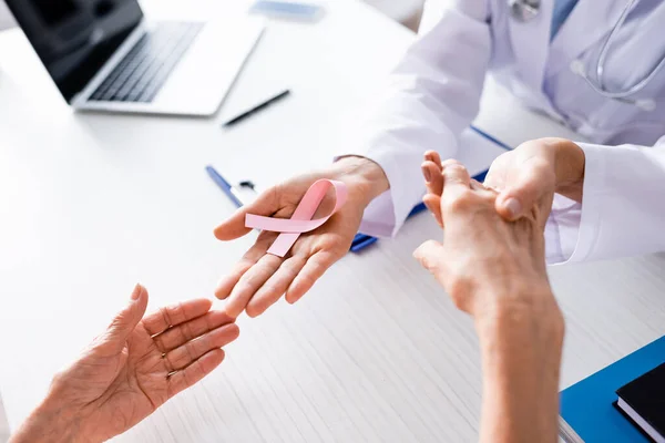 Vue recadrée du médecin tenant les mains du patient et montrant un ruban rose — Photo de stock