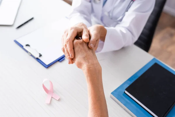 Enfoque selectivo del médico sosteniendo la mano del paciente cerca de la cinta rosa en la mesa — Stock Photo