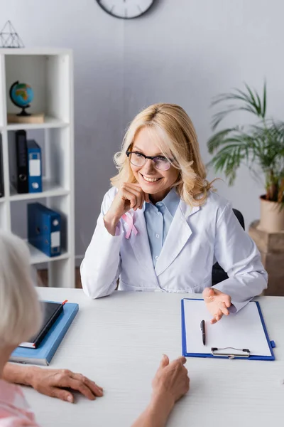Selective focus of doctor with pink ribbon talking to patient near clipboard — Stock Photo