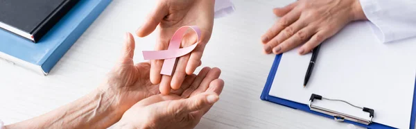 Foto panorámica de médico y paciente sosteniendo cinta rosa en las manos en el lugar de trabajo - foto de stock