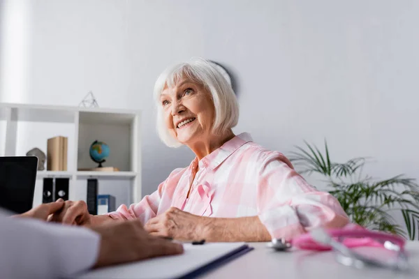 Selective focus of elderly woman holding hand with doctor while sitting at table — Stock Photo