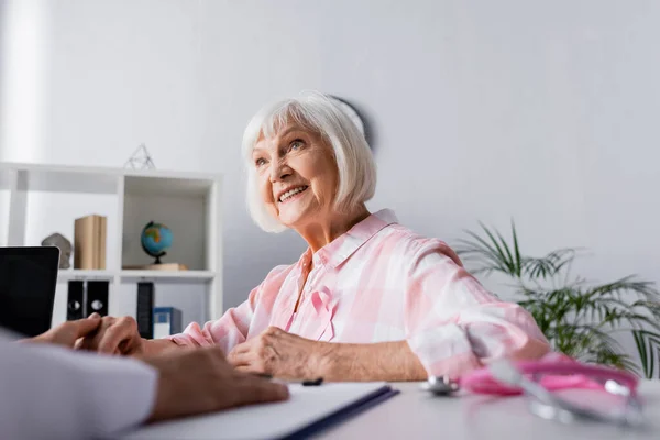 Focus selettivo della donna anziana che tiene la mano con il medico mentre si siede a tavola — Foto stock