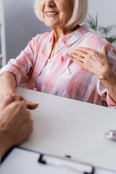 Cropped view of elderly woman with hand on breast near pink ribbon — Stock Photo