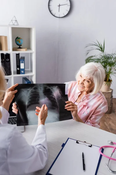 Doctor and elderly woman holding and looking at chest x-ray at workplace — Stock Photo