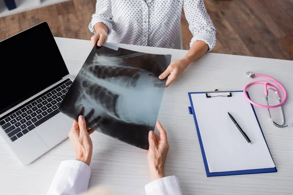 Cropped view of young adult woman and doctor holding x-ray near laptop on table — Stock Photo