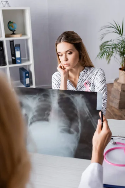 Селективный фокус грустной молодой женщины, сидящей рядом с доктором с рентгеном груди — стоковое фото