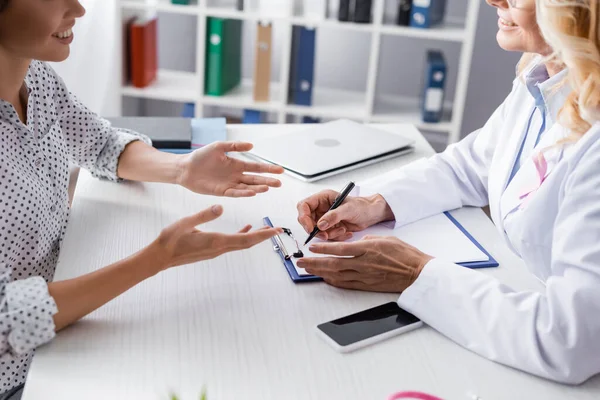 Cropped view of patient and doctor writing on clipboard at workplace — Stock Photo