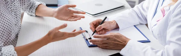 Panoramaaufnahme von Patient und Arzt beim Schreiben auf Klemmbrett am Arbeitsplatz — Stockfoto