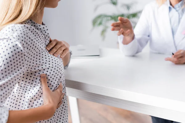 Focus selettivo della giovane donna adulta con le mani sul seno seduta vicino al medico — Foto stock