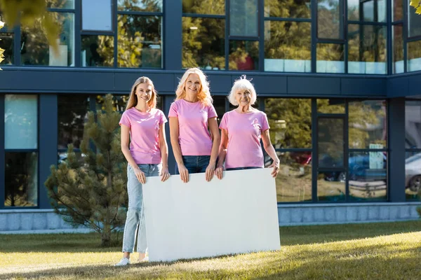 Three women in pink t-shirts with empty board, concept of breast cancer — Stock Photo