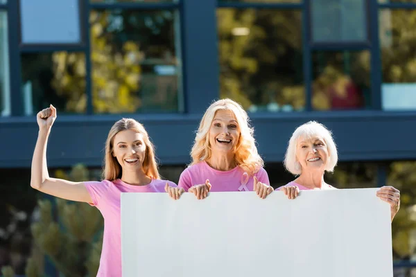 Mulheres excitadas segurando placa vazia com edifício no fundo — Fotografia de Stock