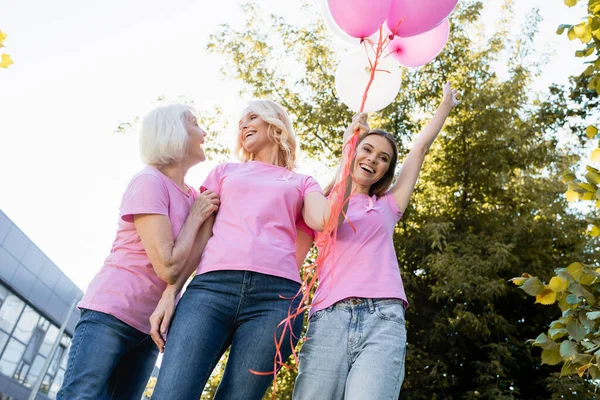 Низкий угол обзора женщин в розовых футболках с розовыми лентами, держащих воздушные шары — стоковое фото