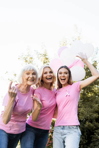 Trois femmes excitées avec des rubans roses tenant des ballons à l'extérieur — Photo de stock