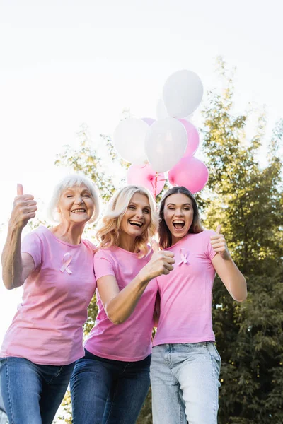 Femmes excitées avec les pouces levés près des ballons, concept de cancer du sein — Photo de stock