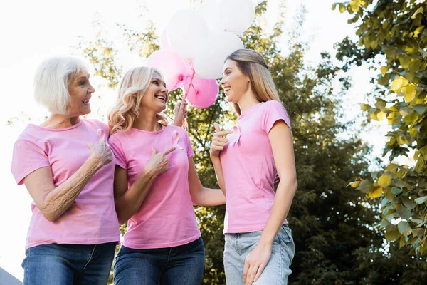 Vista de ángulo bajo de las mujeres que señalan con los dedos a las cintas de color rosa, sosteniendo globos - foto de stock