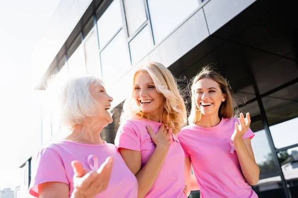 Mujeres en camisetas rosas riendo y abrazándose al aire libre, concepto de cáncer de mama - foto de stock