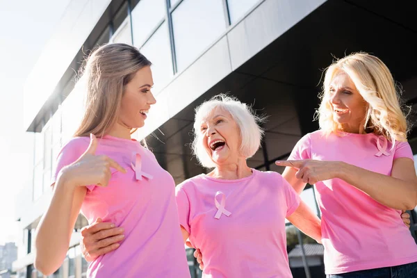 Women laughing and pointing with fingers at sign of breast cancer awareness — Stock Photo