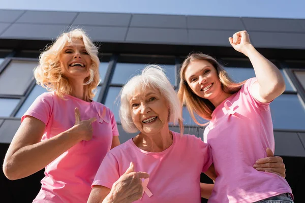 Low angle view of women hugging and pointing with fingers at pink ribbons — Stock Photo