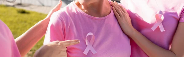 Panoramic shot of woman pointing with finger at pink ribbon on woman's t-shirt — Stock Photo