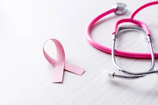 Fita rosa de consciência de câncer de mama perto de estetoscópio em fundo de madeira branca — Fotografia de Stock