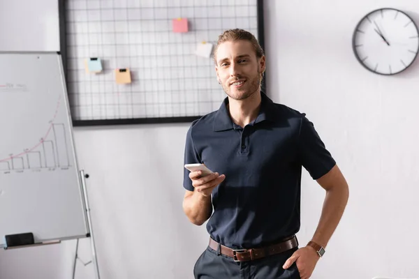 Happy office worker with hand in pocket looking at camera while standing at workplace — Stock Photo