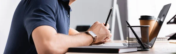 Обрізаний вид бізнесмена з ручкою, що сидить за робочим столом біля ноутбука на розмитому фоні, банер — стокове фото