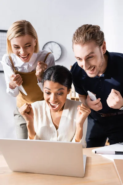 Feliz gente de negocios multicultural con sí gestos mirando a la computadora portátil en la oficina - foto de stock