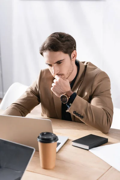 Pensativo jovem adulto em desgaste formal olhando para laptop na mesa no escritório — Fotografia de Stock