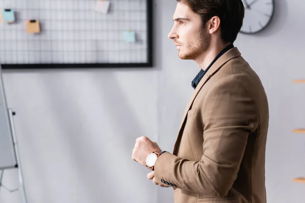 Бічний вид упевненого бізнесмена стоячи і озираючись, а пряме рукав куртки в офісі на розмитому тлі — стокове фото