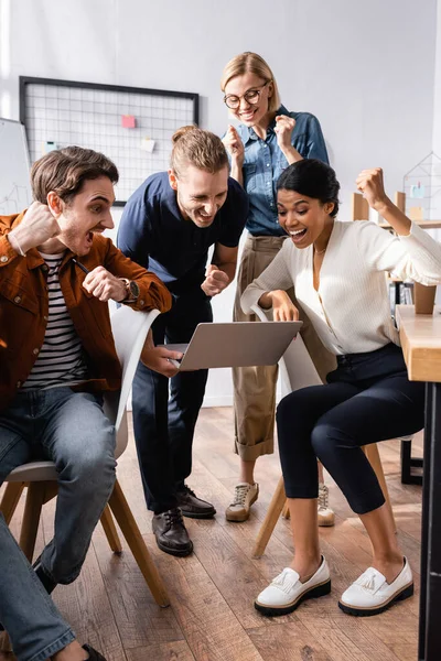 Empresarios multiculturales emocionados gritando y mostrando gesto de éxito mientras mira el ordenador portátil - foto de stock