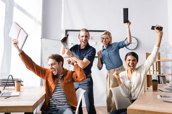 Excited multicultural businesspeople shouting and showing success gesture in office — Stock Photo