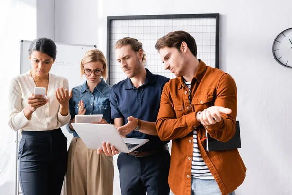 Serio uomo d'affari che punta al computer portatile vicino a colleghi multiculturali scontenti — Foto stock