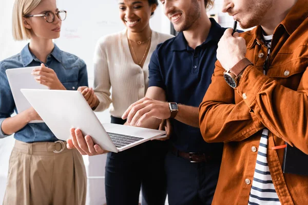 Gerente feliz usando laptop perto de amigos multiculturais no escritório — Stock Photo