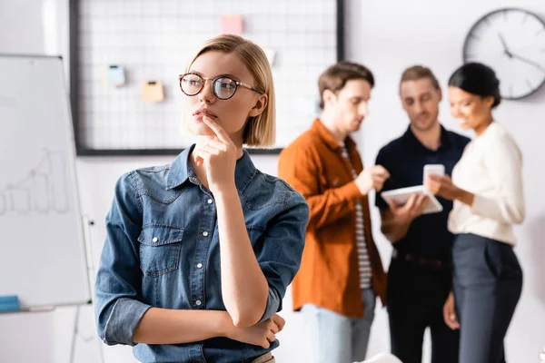 Gérant blond réfléchissant tout en détournant les yeux, et des collègues multiethniques communiquant sur fond flou — Photo de stock