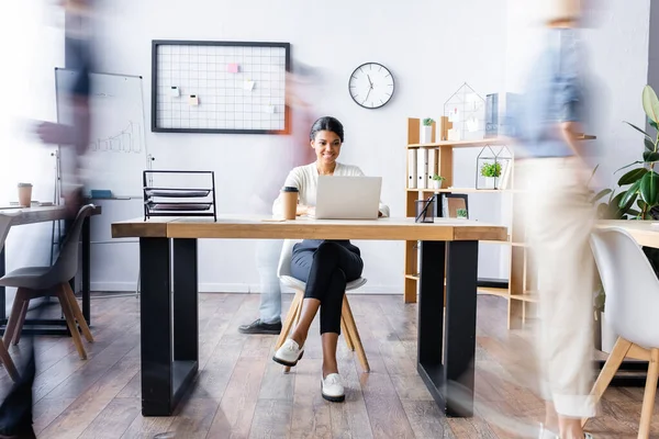 Happy african american manager working at laptop in open space office, motion blur — Stock Photo