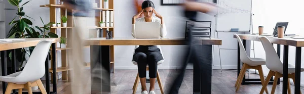 Cansada mujer de negocios afroamericana tocando la cabeza mientras sufre de dolor de cabeza en la oficina de espacio abierto, pancarta, desenfoque de movimiento - foto de stock