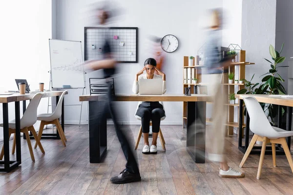 Exhausted african american businesswoman touching head while suffering from migraine in open space office, motion blur — Stock Photo