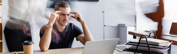 Exhausted businessman suffering from headache while sitting at workplace in open space office, banner — Stock Photo