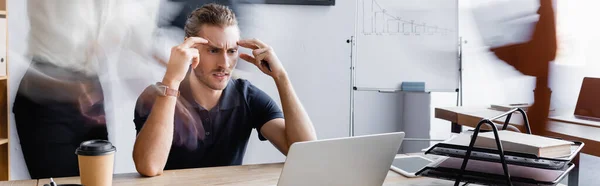 Uomo d'affari esausto che soffre di mal di testa mentre seduto sul posto di lavoro in ufficio open space, banner — Foto stock