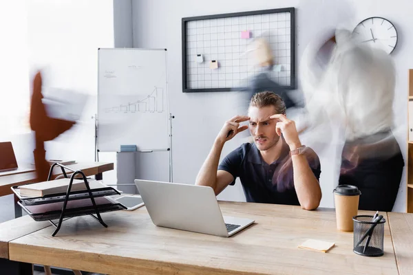 Stanco uomo d'affari che soffre di emicrania mentre lavora in ufficio open space, movimento sfocatura — Foto stock