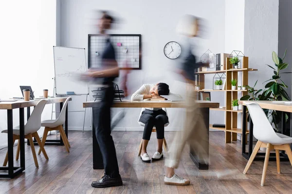 Femme d'affaires afro-américaine épuisée dormant sur le bureau dans un bureau ouvert, flou de mouvement — Photo de stock